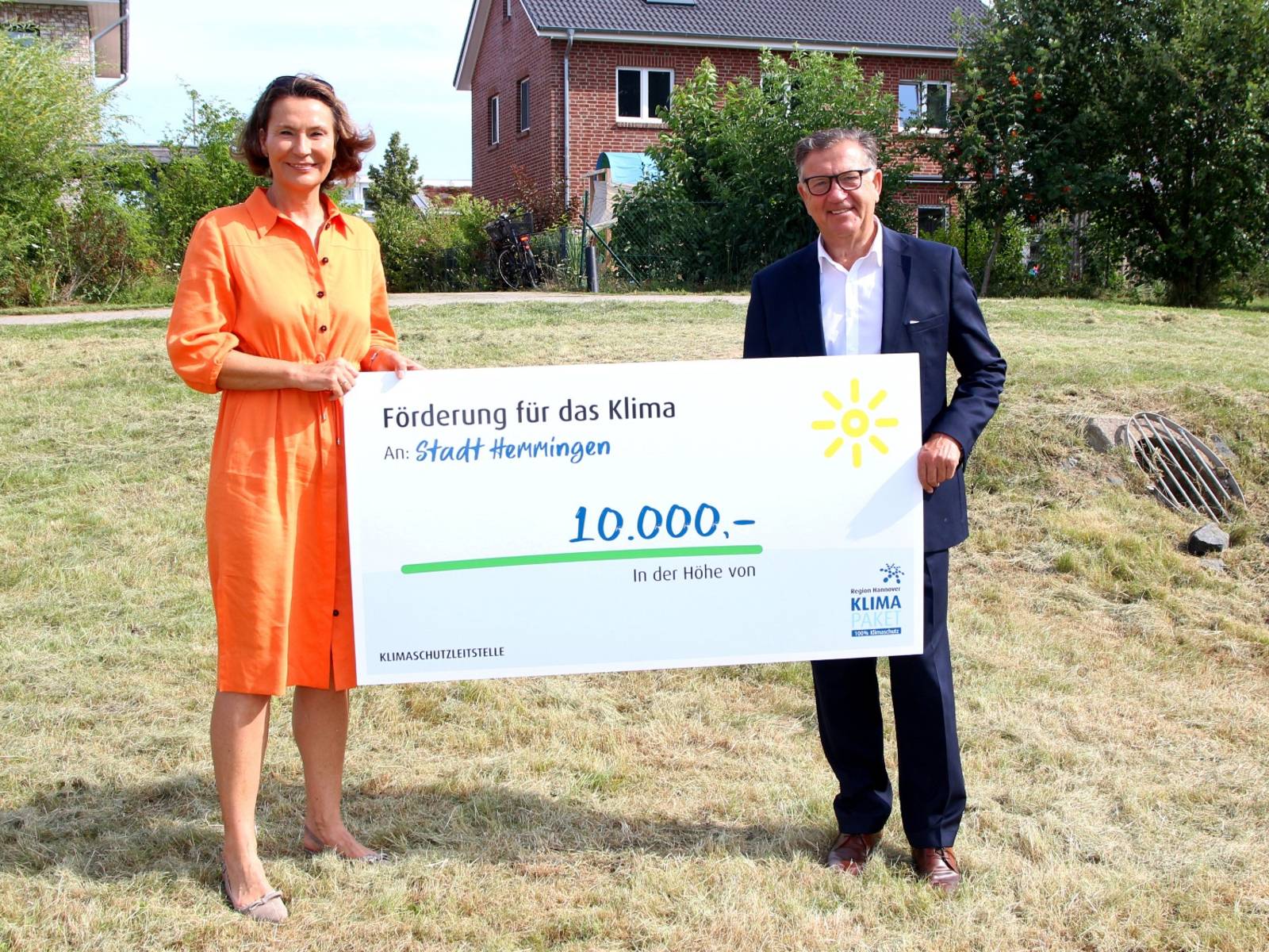 Eine Frau und ein Mann halten einen symbolischen Scheck in Höhe von 10.000 Euro